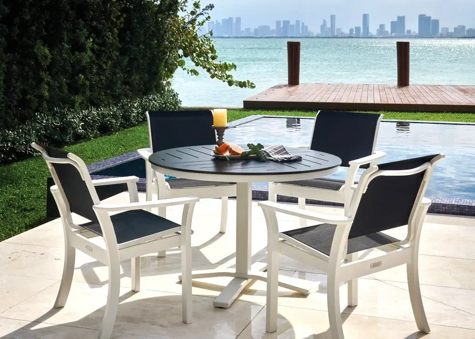 Commercial outdoor dining set with sling armchairs and a round table overlooking a luxury waterfront pool and marina view.